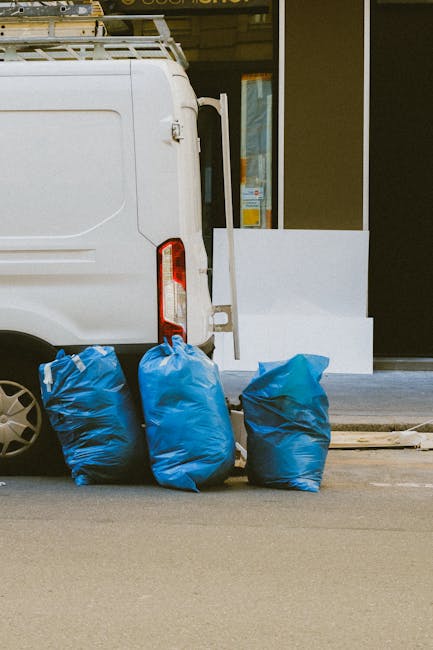 A large pile of neatly stacked blue and white paper documents and files is situated on the pavement outside a building with a stone facade. The documents appear to be a mix of manila folders and loose